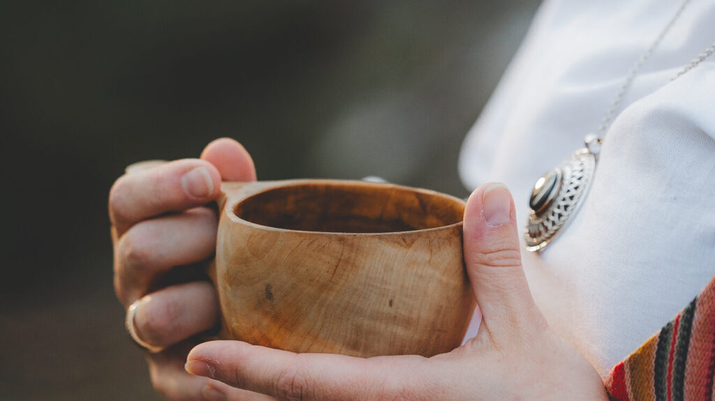 Kreetta holding a kuksa -cup filled with coffee wearing national costume.