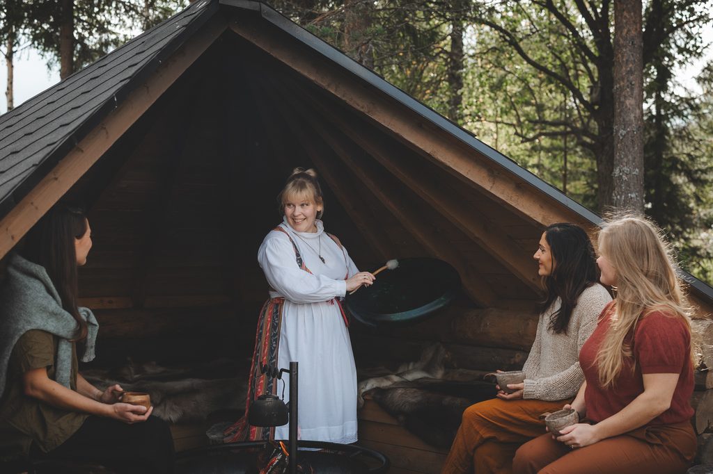 Singer sharing a meaningful Finnish cultural experience with women in a traditional kota in Rovaniemi.